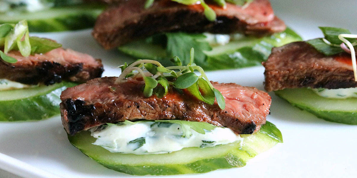 Strip steak in a Spicy Asian sauce, herbed cream cheese, and toppings on a cucumber slice.